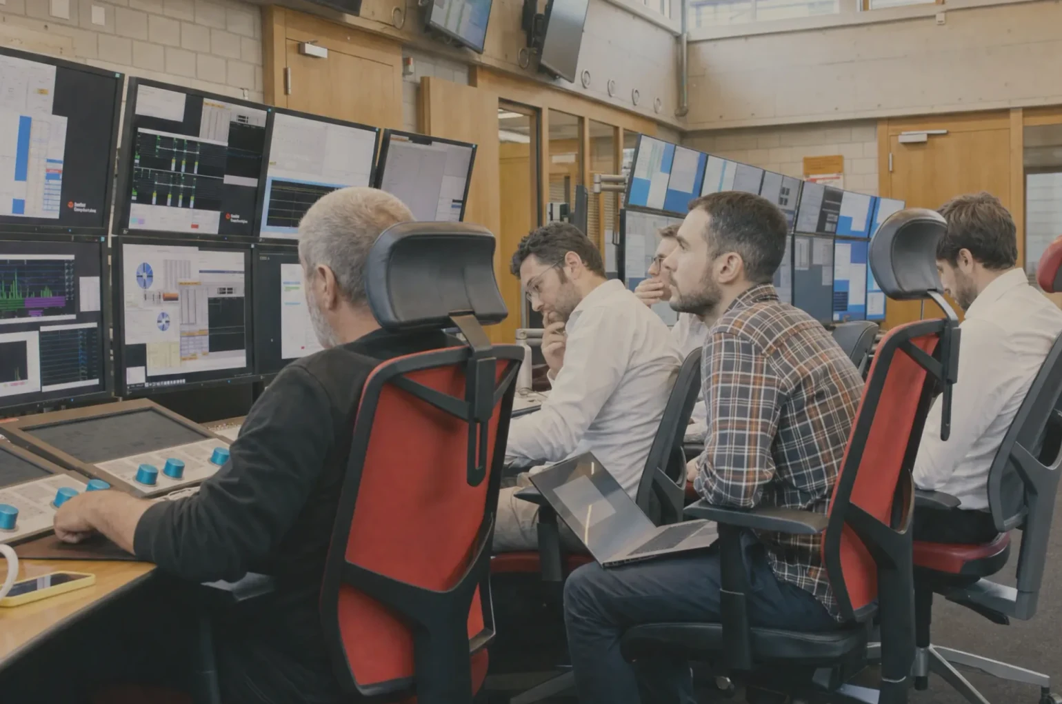 Two colleagues collaborating beside control-room monitors.